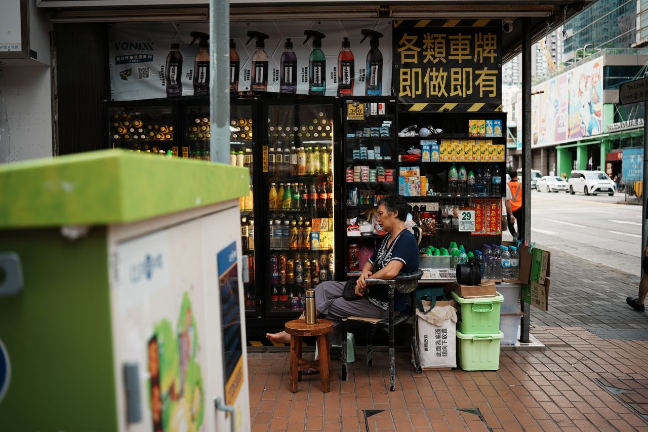 A local vendor sits at a bustling street kiosk selling drinks and snacks in an urban environment.